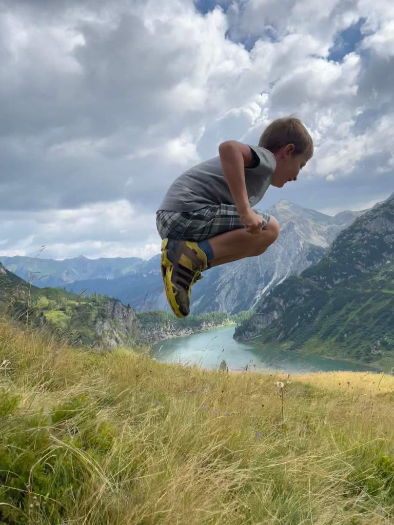 Wanderung zum Tappenkarsee, David springt fröhlich über eine Wiese mit Bergblick in Kleinarl. Familienurlaub genießen!