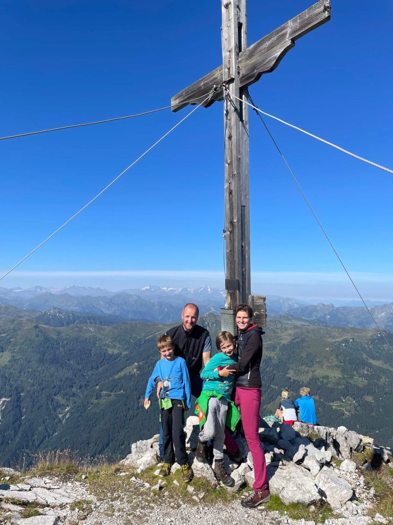 Familie Viehhauser am Gipfel des Ennskrax Bergkreuz und Panorama der Salzburger Alpen im Hintergrund.