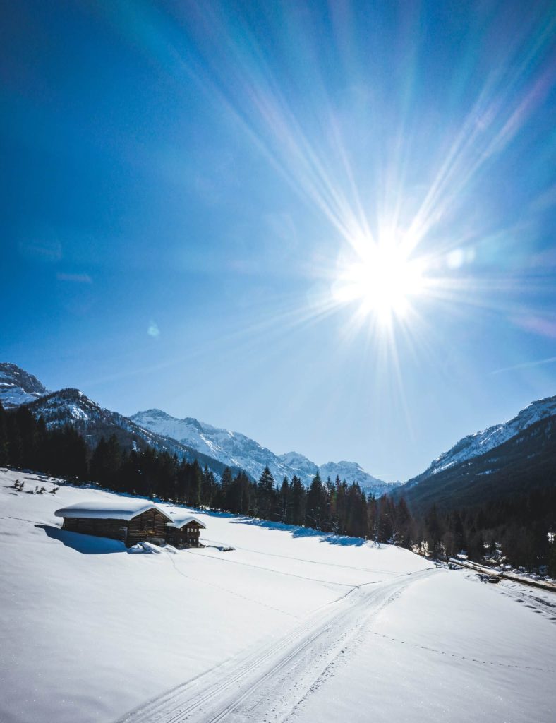 Winterliche Landschaft mit verschneitem Bauernhof und Bergen unter klarem blauen Himmel.
