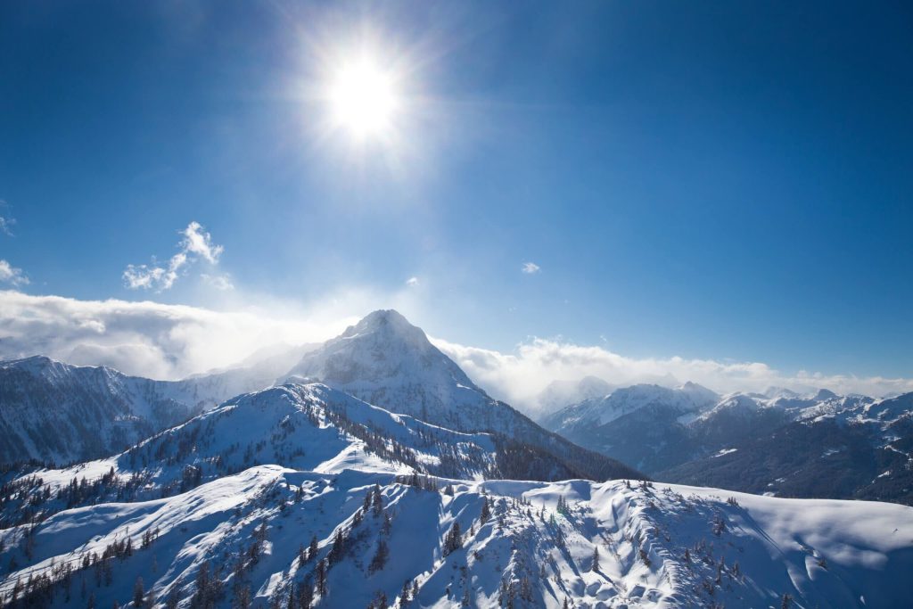 Schneebedeckte Berge unter klarem Himmel und strahlender Sonne in den Salzburger Alpen.